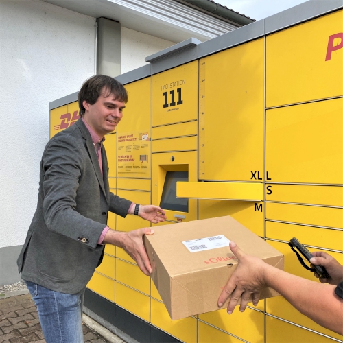 Andreas Mehltretter legt im Rahmen einer Tour mit einem Paketzusteller von DHL ein Paket in eine DHL-Packstation